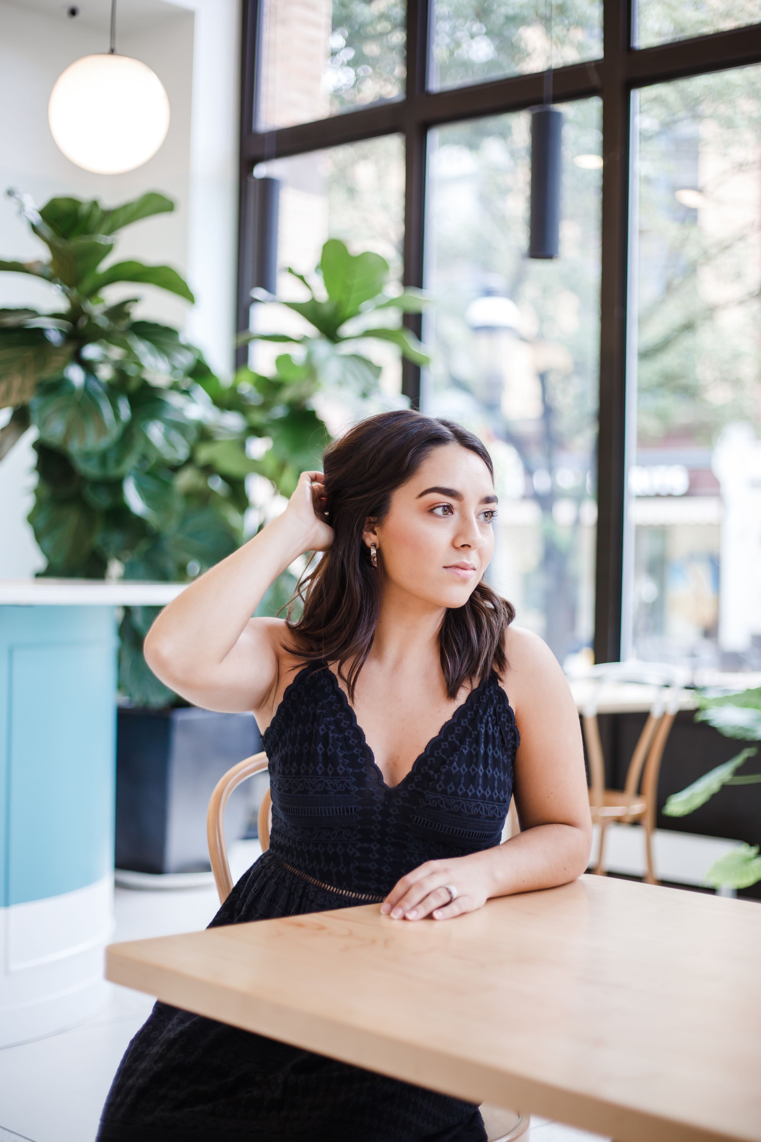 Indoor portraits at a modern cafe with large windows and plants, featuring casual poses at a wooden table.
