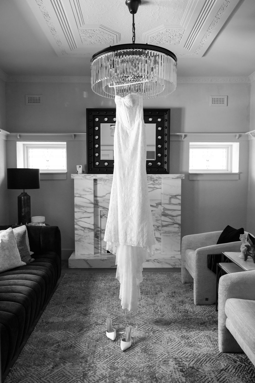White wedding dress hanging from chandelier in elegant room with gray walls.