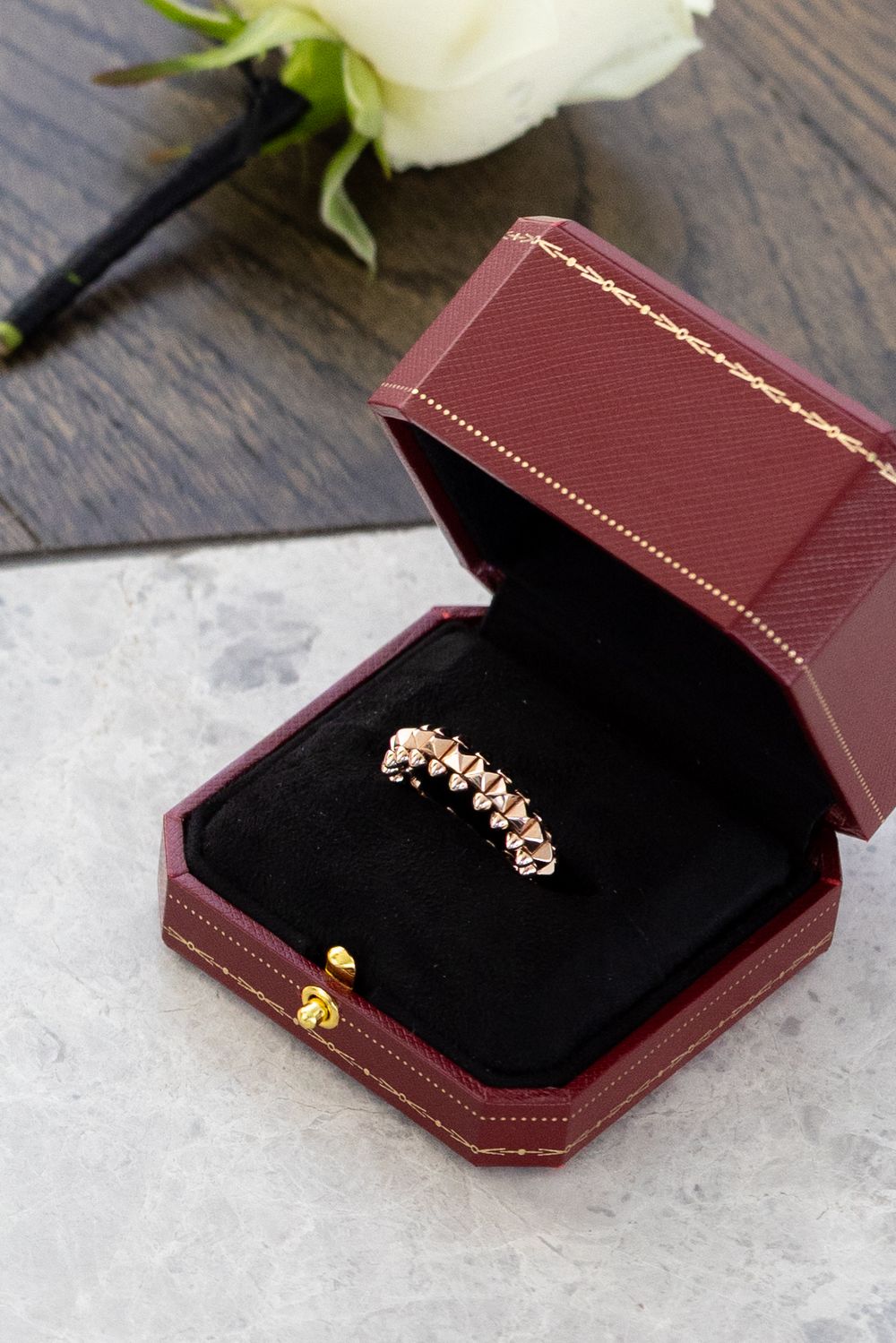 Delicate rose gold jewelry displayed in burgundy ring box on wooden surface.