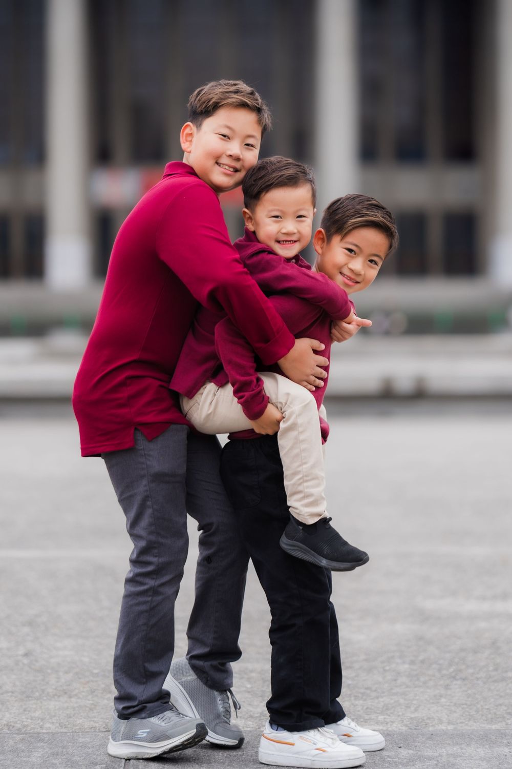 Three people wearing matching burgundy sweaters embrace and laugh together outdoors.