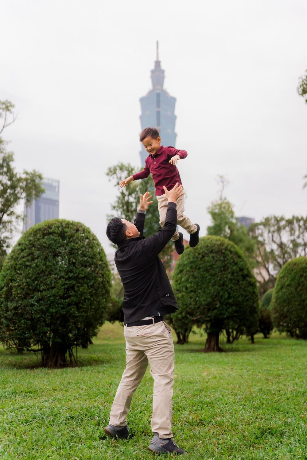 People playing and having fun in a grassy park area with Taipei 101 tower visible in the distance.