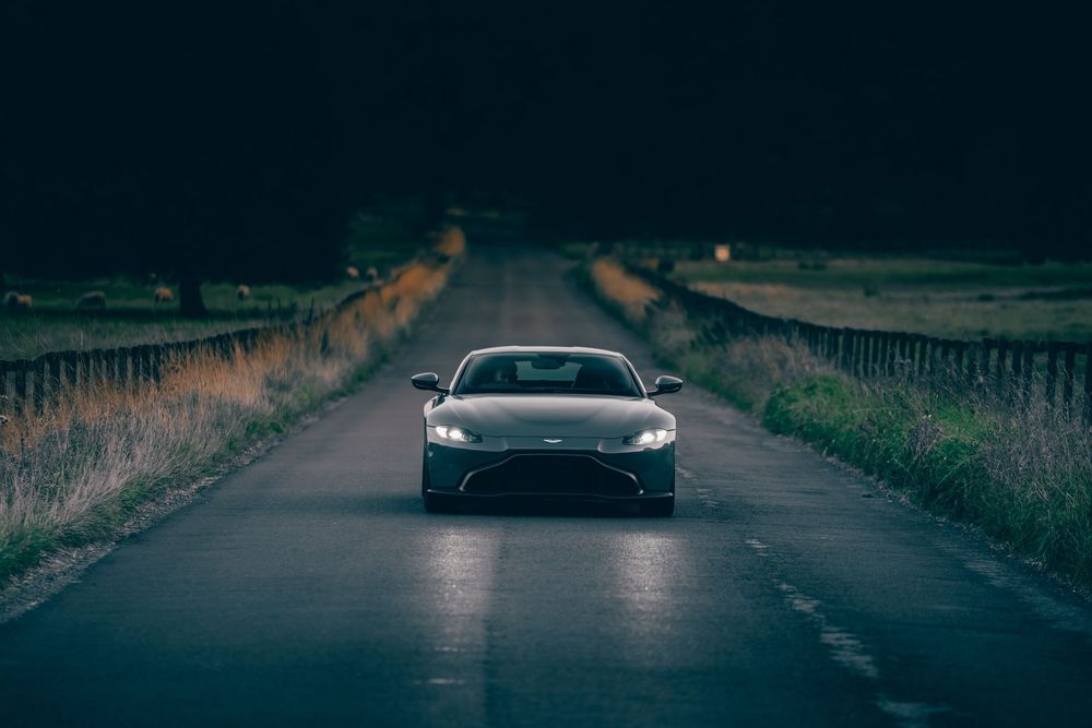 A silver sports car is parked on a dark rural road at dusk with dramatic moody lighting.