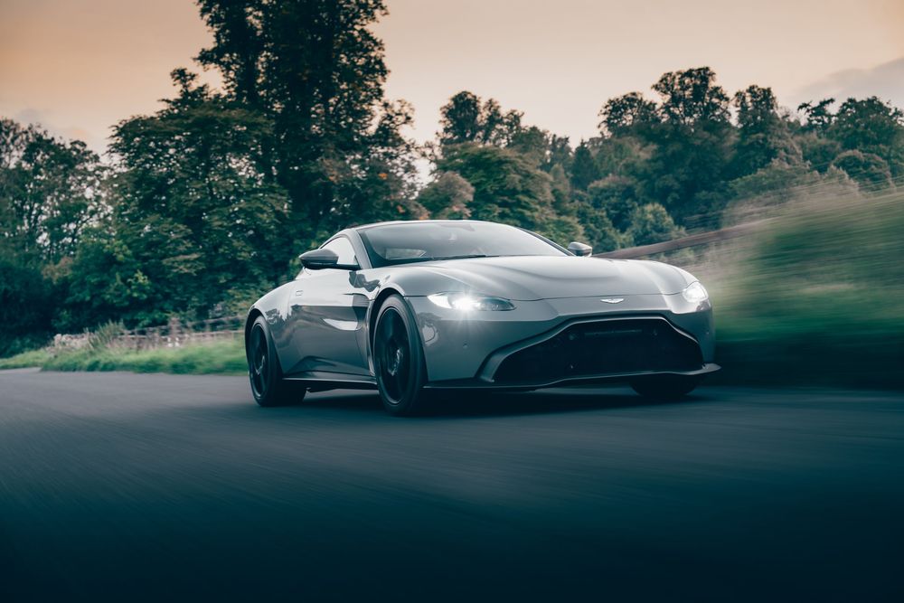 A sleek silver sports car drives through a misty forest road during twilight hours.