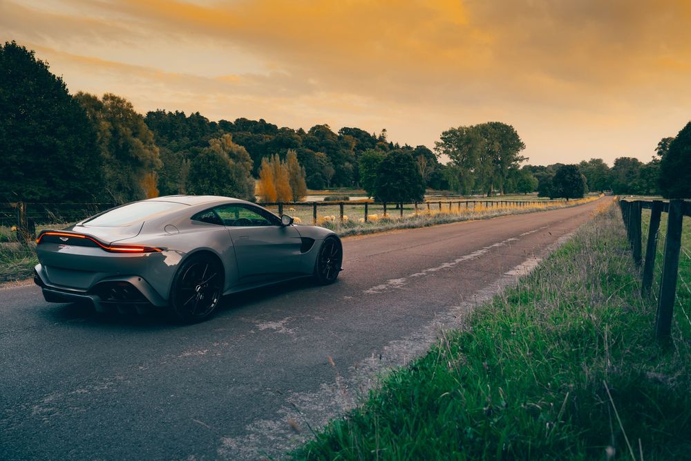 Rear view of luxury sports car parked on country road with wooden fencing and dramatic orange sky.