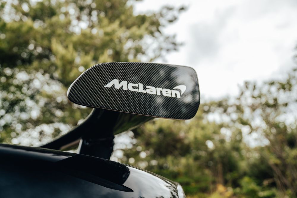 A black McLaren supercar with an active rear wing spoiler system on display in an outdoor setting.
