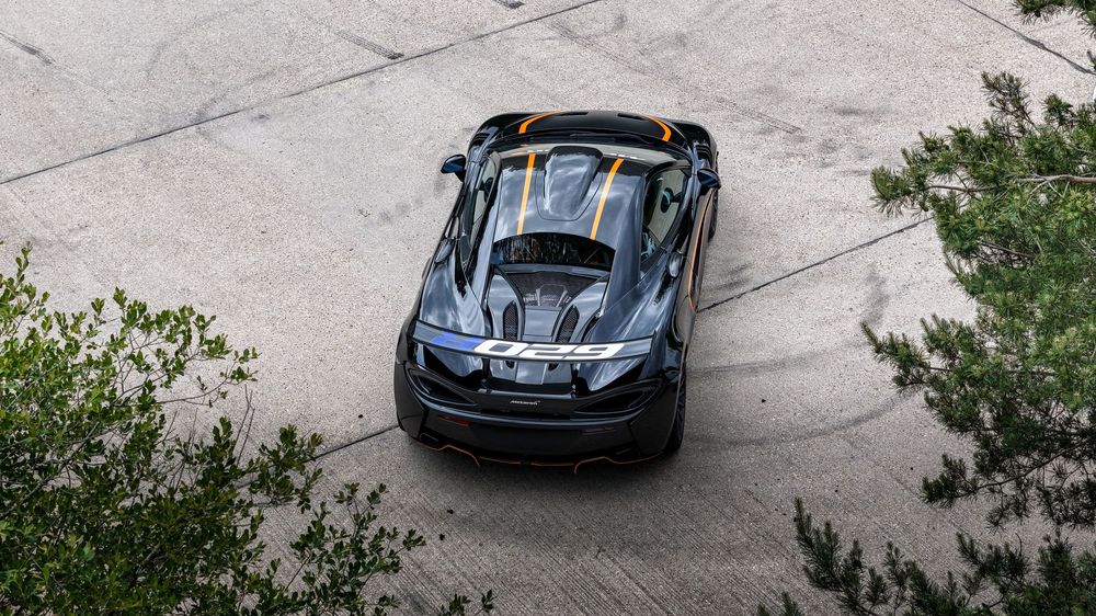 Aerial view of a black sports car driving along a curved concrete road surrounded by green foliage.
