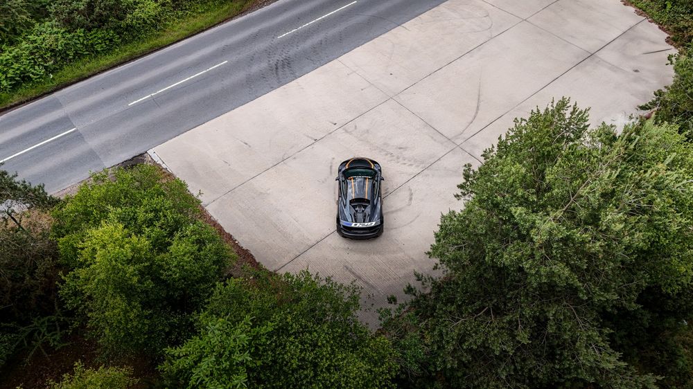 Bird's eye perspective of a luxury vehicle navigating a winding road through lush greenery.