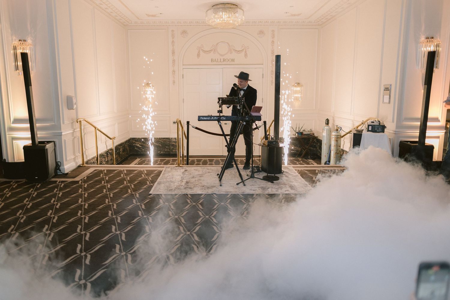 Fog or smoke fills an elegant white room with ornate moldings and chandeliers during what appears to be a film shoot.