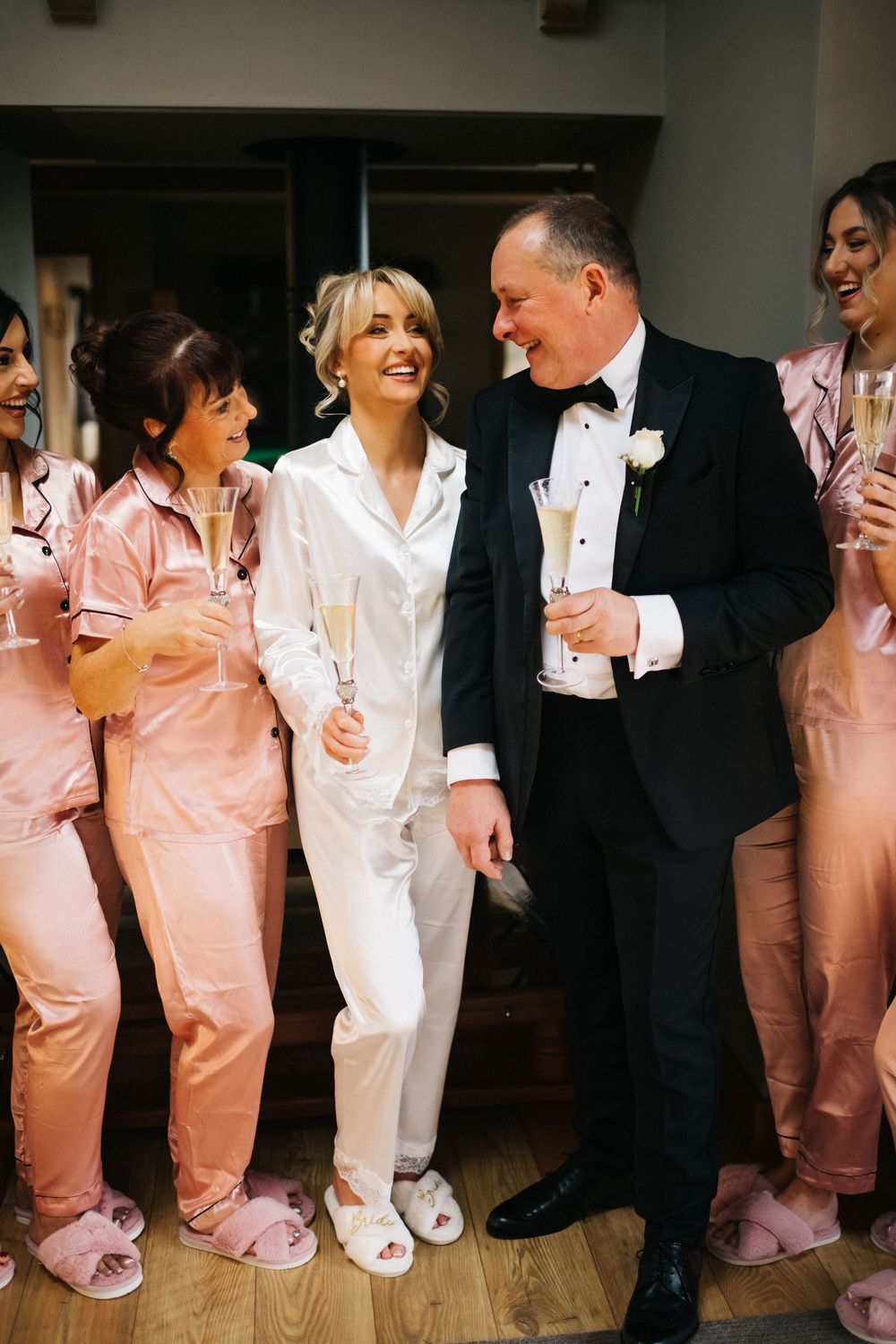 Wedding party members wearing matching pink and white pajamas pose together on hardwood floor.
