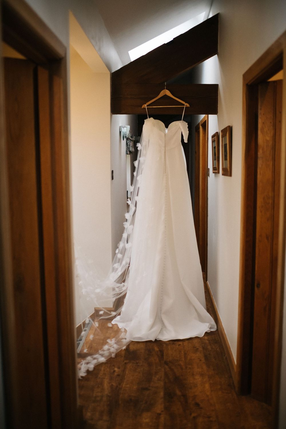 White wedding dress hanging in a dimly lit hallway with wooden doors and frames.