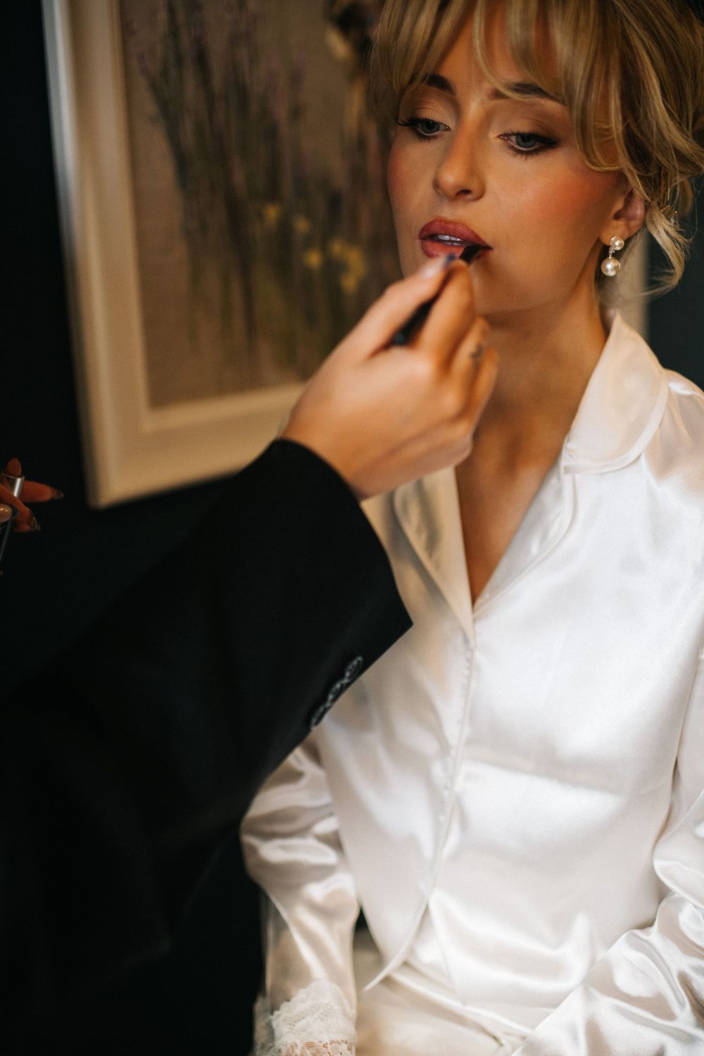 Close-up shots of a bride getting ready in a white silk robe with elegant makeup and styled hair.