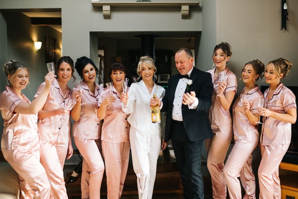 Wedding party in pink bridesmaid dresses and formal attire pose together in a line against a dark wall.