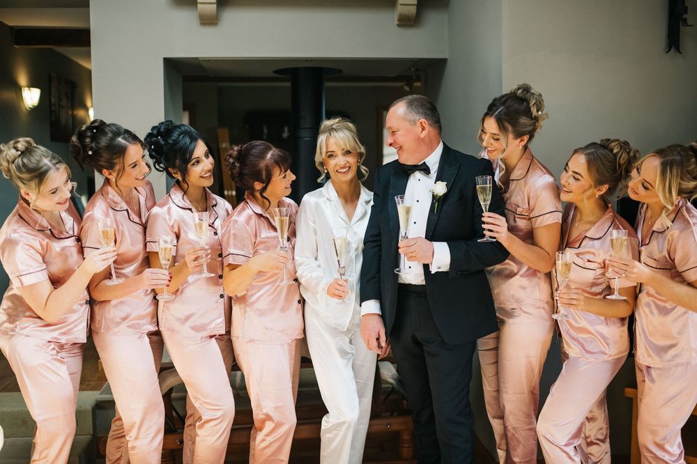 Wedding party members in matching pink dresses and dark suits line up for a fun group photo at a reception.