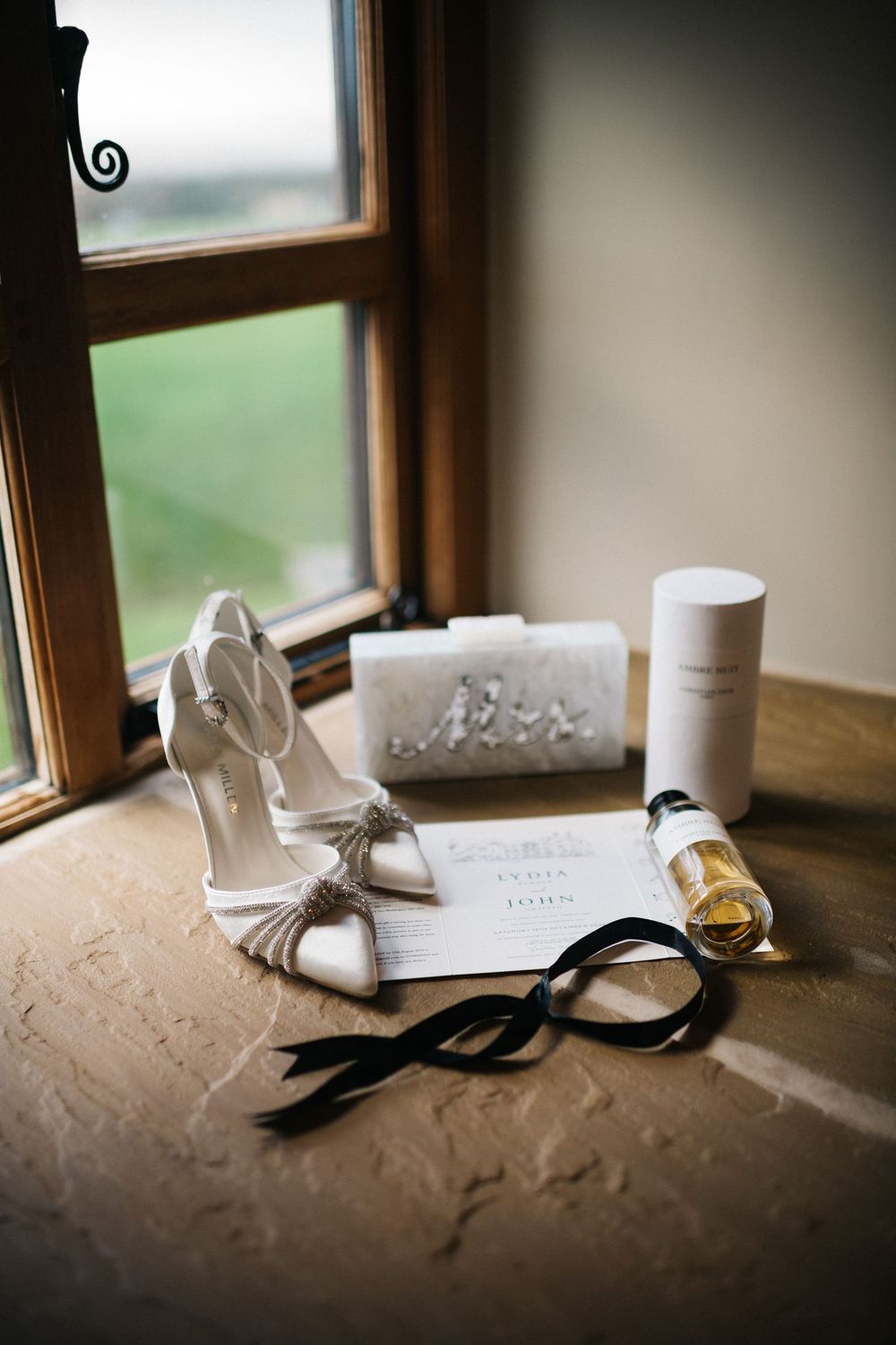 Wedding accessories including white shoes and black bow tie arranged by window.