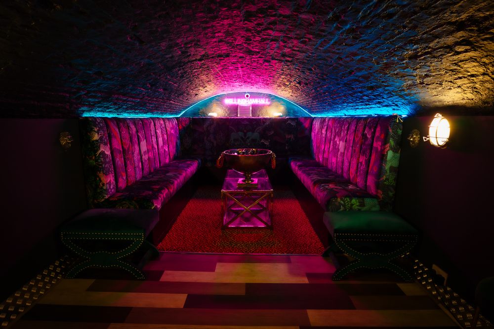 Brick archway venue space illuminated by dramatic pink and blue lighting effects. Ellingham Hall