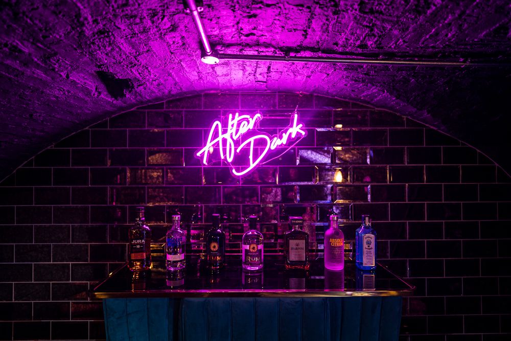 Dark brick-walled bar space with glowing pink neon signage and ambient lighting. Ellingham Hall
