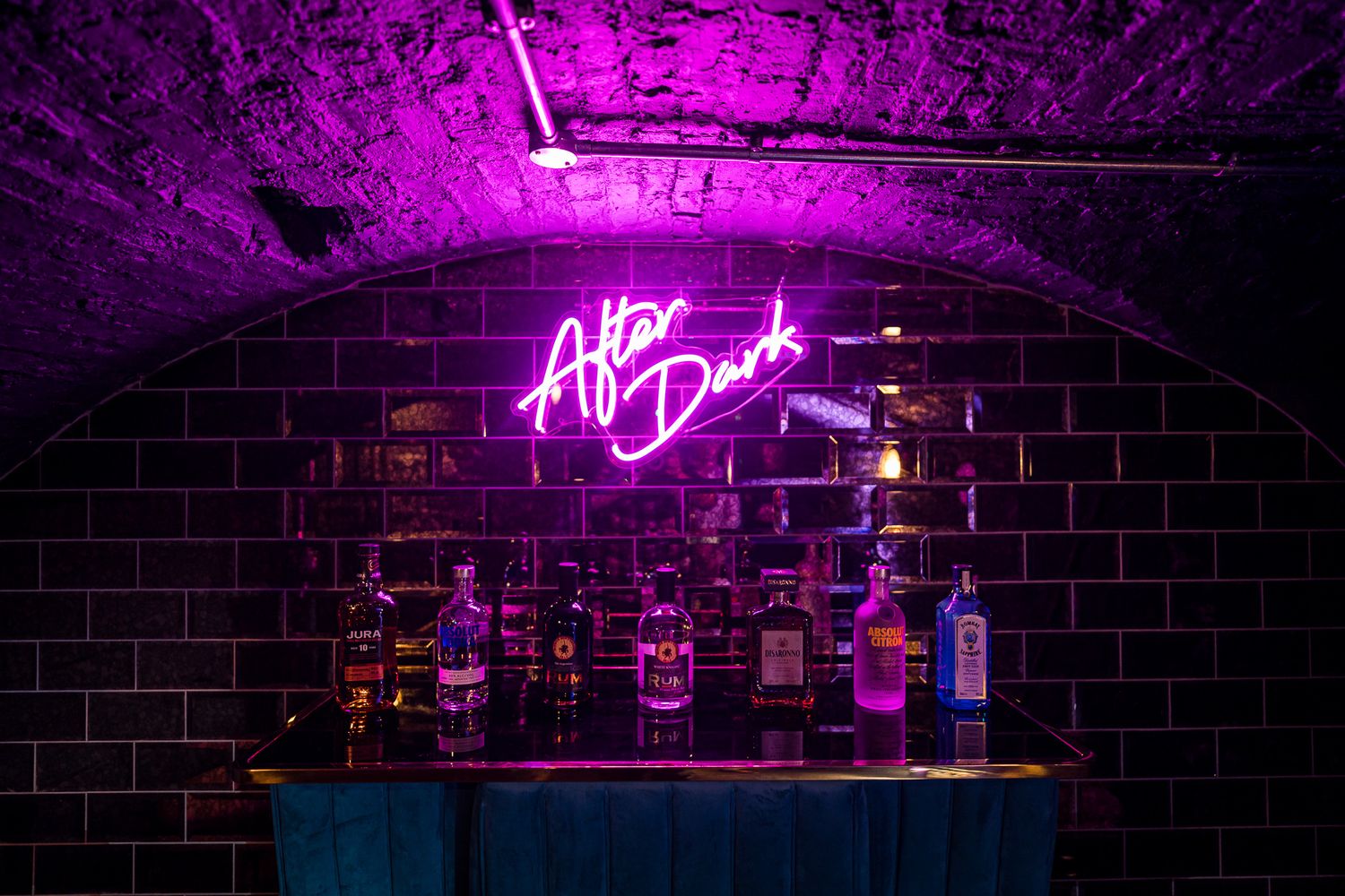 Dark brick-walled bar space with glowing pink neon signage and ambient lighting. Ellingham Hall