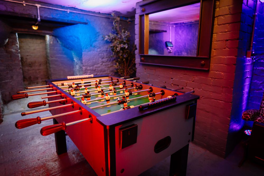 Game room with foosball tables lit by dramatic purple and blue accent lighting. Ellingham Hall