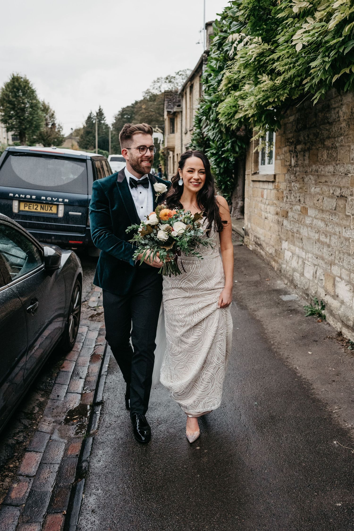 A couple walking down a stone-walled street in formal attire on a rainy day.