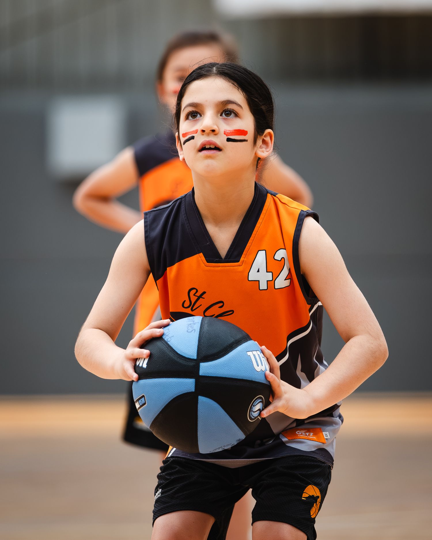 Youth basketball players in orange and black uniforms playing defense during a game.
