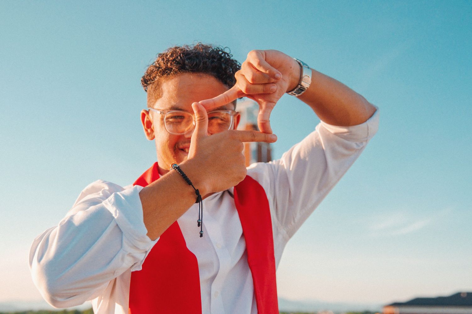 Person in red vest and white shirt making expressive faces against blue sky background.