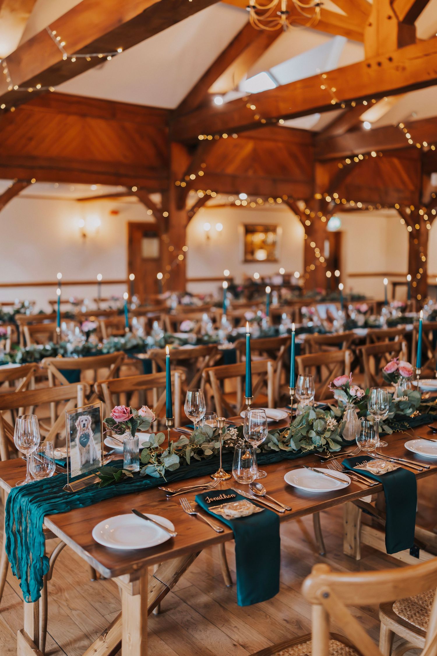 Rustic wedding reception venue with wooden beams, teal table runners and string lights decorating elegant table settings.