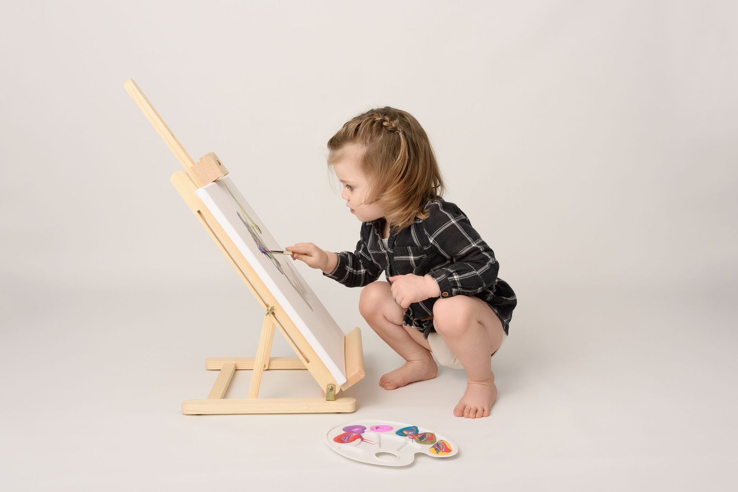 Picasso shoot! Creative baby photography setup with wooden easel and art supplies on white background.