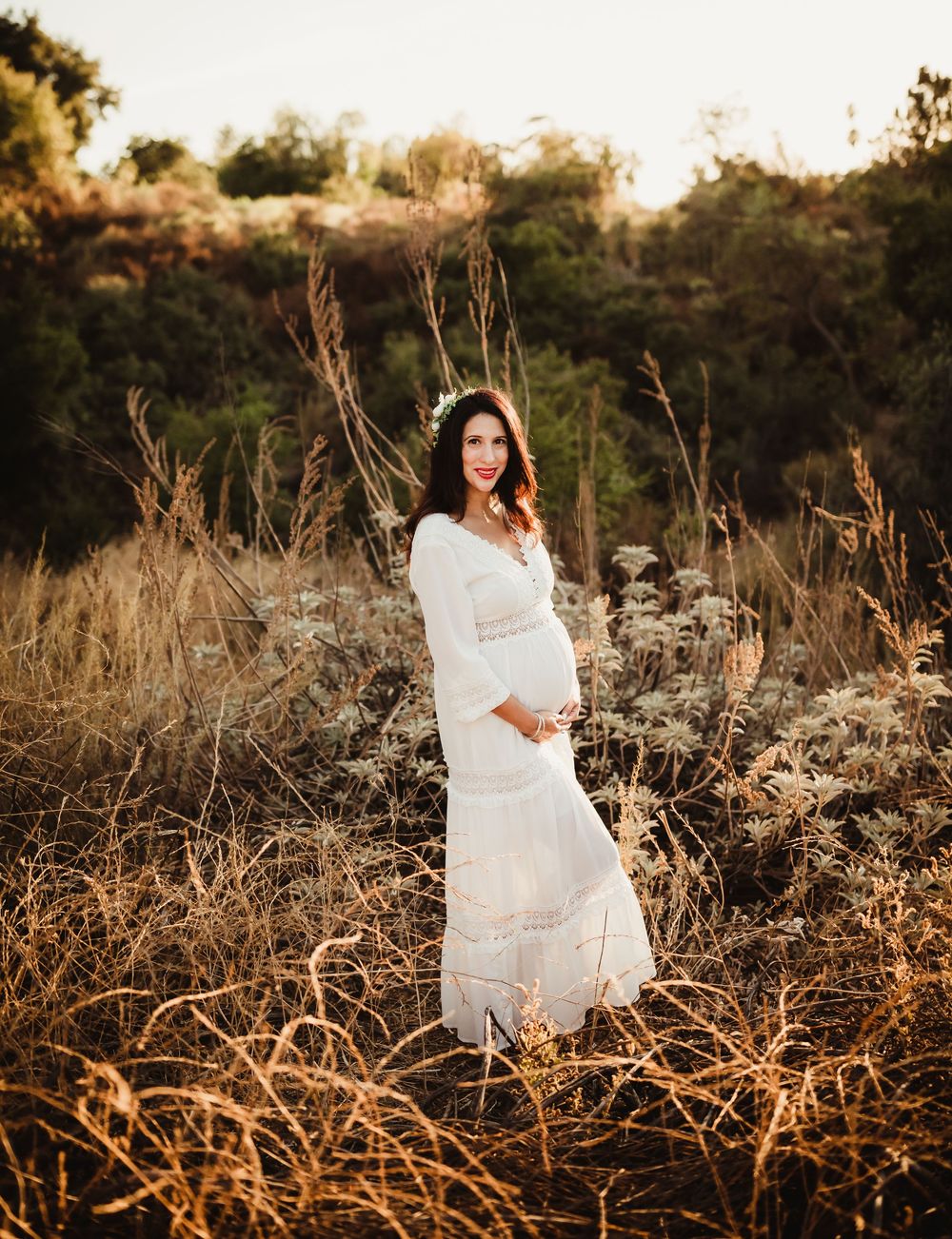 A person in a flowing white dress stands gracefully among tall dried grasses during golden hour.