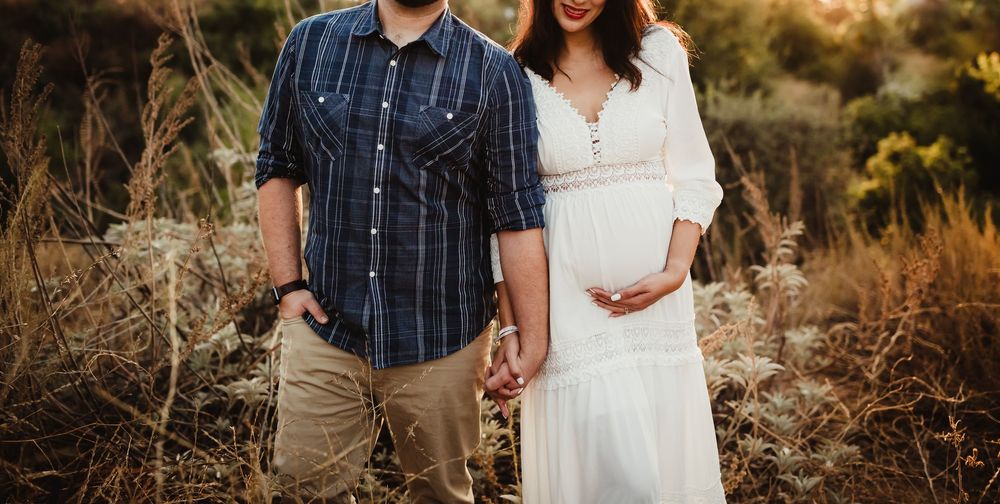 Couple holds hands in golden field during sunset engagement photo session.
