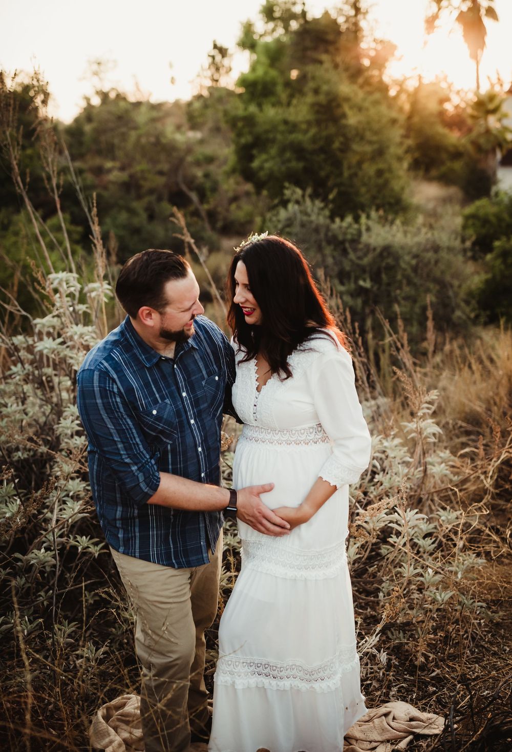 A couple shares an intimate moment during a sunset maternity photoshoot in a natural outdoor setting.