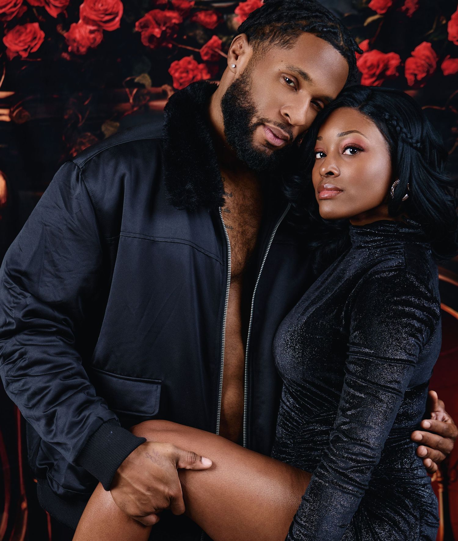 Romantic couple embracing in dark outfits against red floral background.