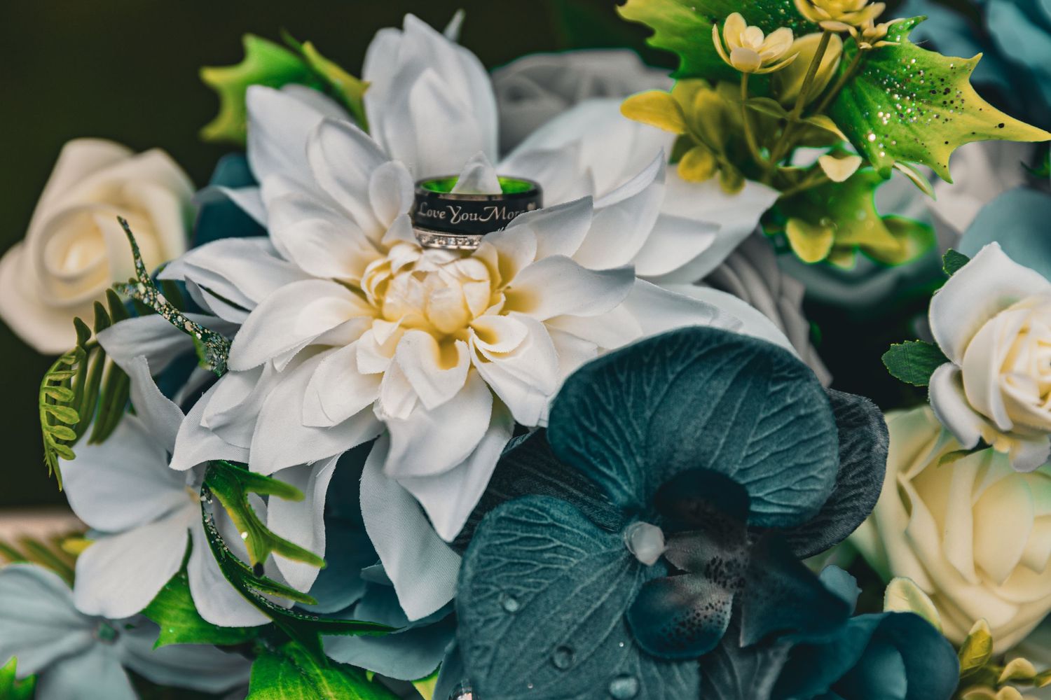 Beautiful wedding ring nestled among lush white dahlias and teal orchids in a bridal bouquet arrangement.
