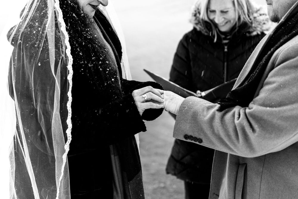 Black and white photo of a wedding ring exchange ceremony with guests witnessing the romantic moment.