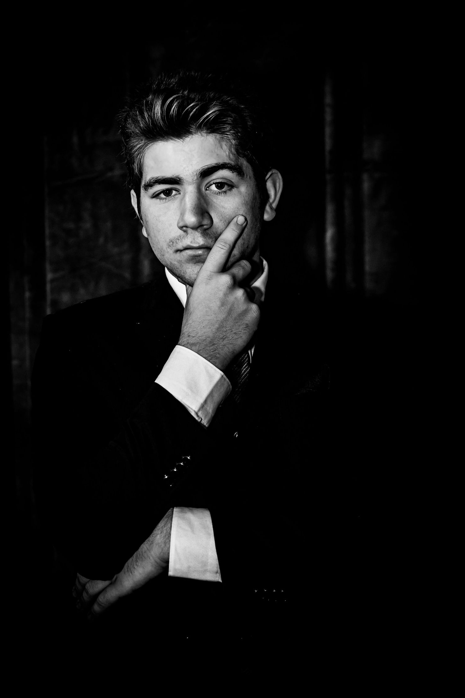 Black and white portrait of a young man in a suit resting his chin on his hand against a dark background.