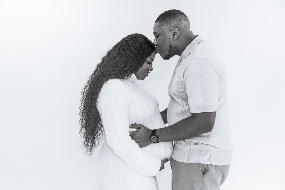 Black and white maternity photo of a couple tenderly touching foreheads while cradling a pregnant belly.