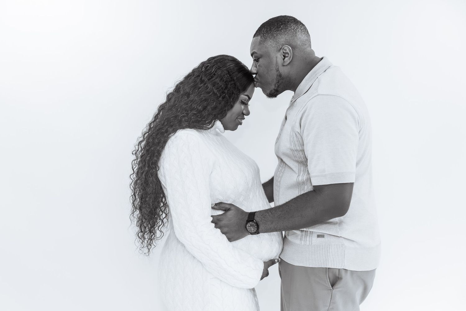 Black and white maternity photo of a couple tenderly touching foreheads while cradling a pregnant belly.