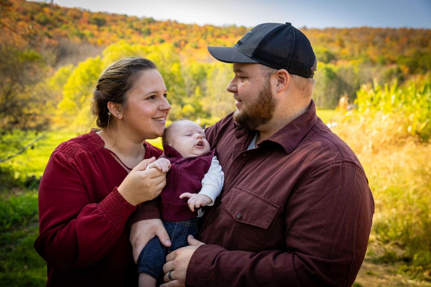 Happy young family with newborn baby enjoying a warm autumn day outdoors in colorful fall landscape.