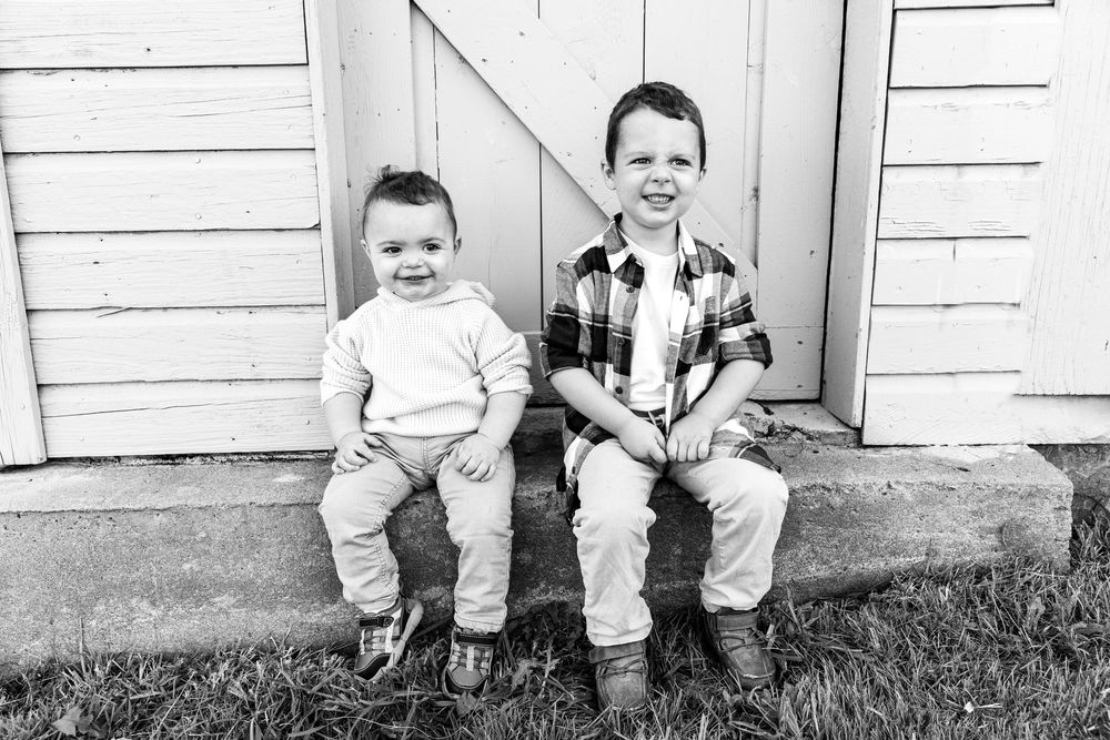 Two young brothers smiling while sitting on steps outside a wooden building, black and white photo.