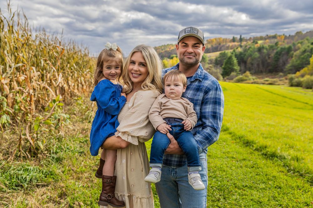 Happy family of four posing beside a cornfield and green meadow on an overcast autumn day.