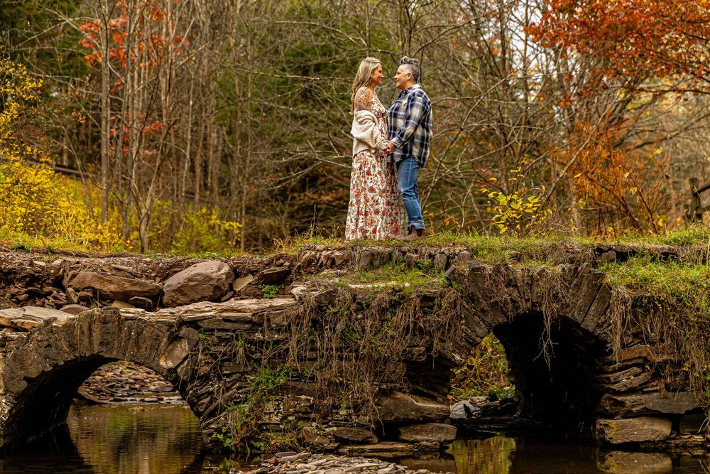 Couple standing on a rustic stone bridge surrounded by colorful autumn foliage during an engagement photo session.