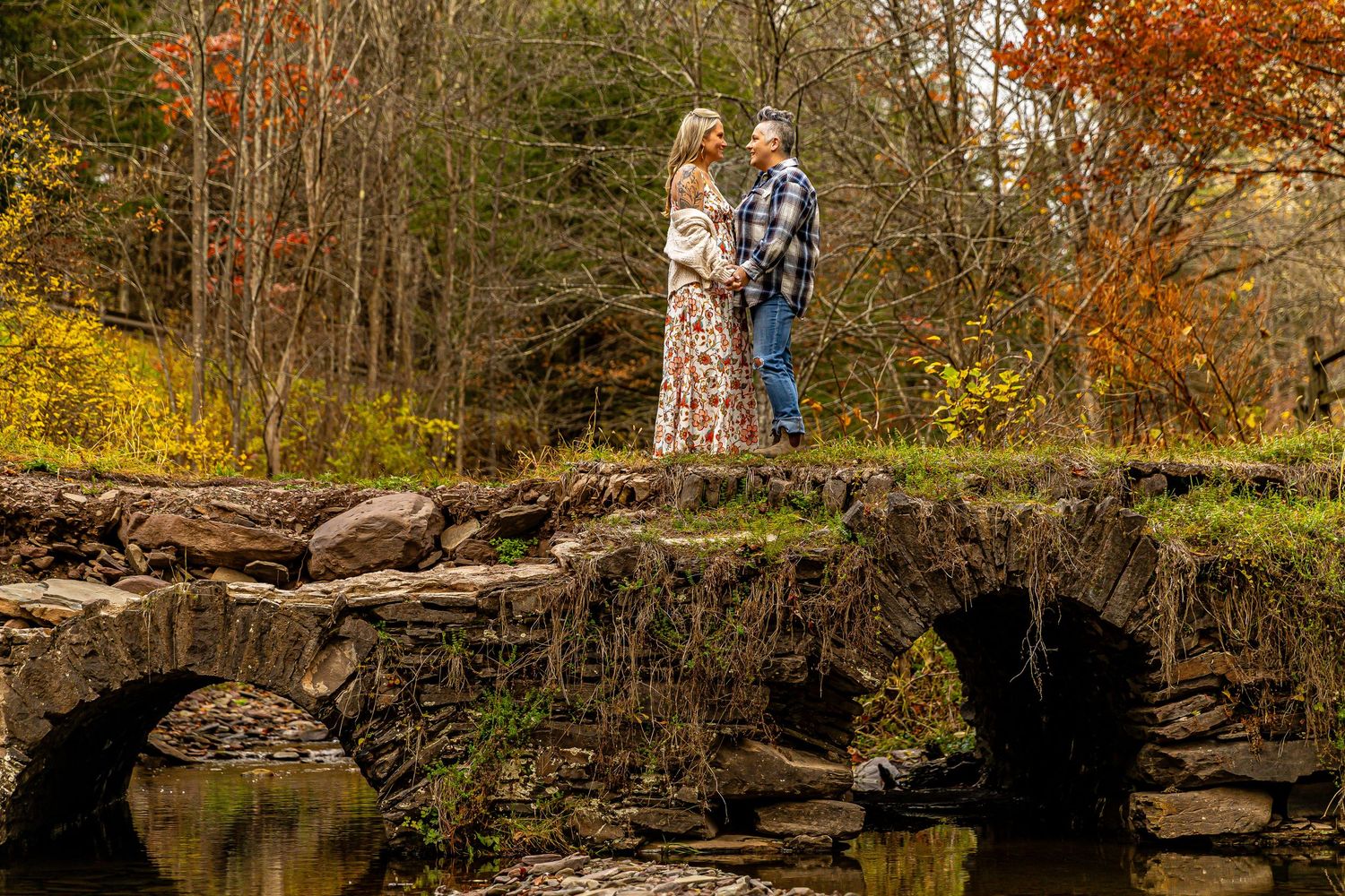 Couple standing on a rustic stone bridge surrounded by colorful autumn foliage during an engagement photo session.