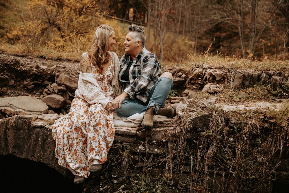 Couple sitting together on rustic stone steps laughing in an autumn woodland setting.