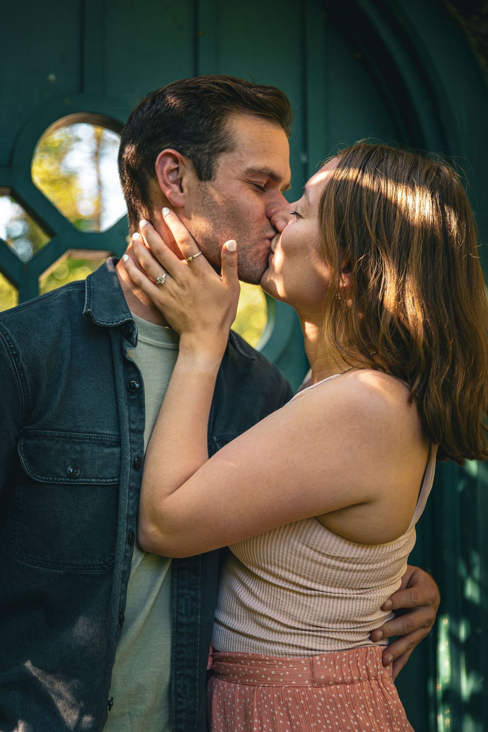 Romantic couple shares a tender kiss in front of a green decorative garden structure.
