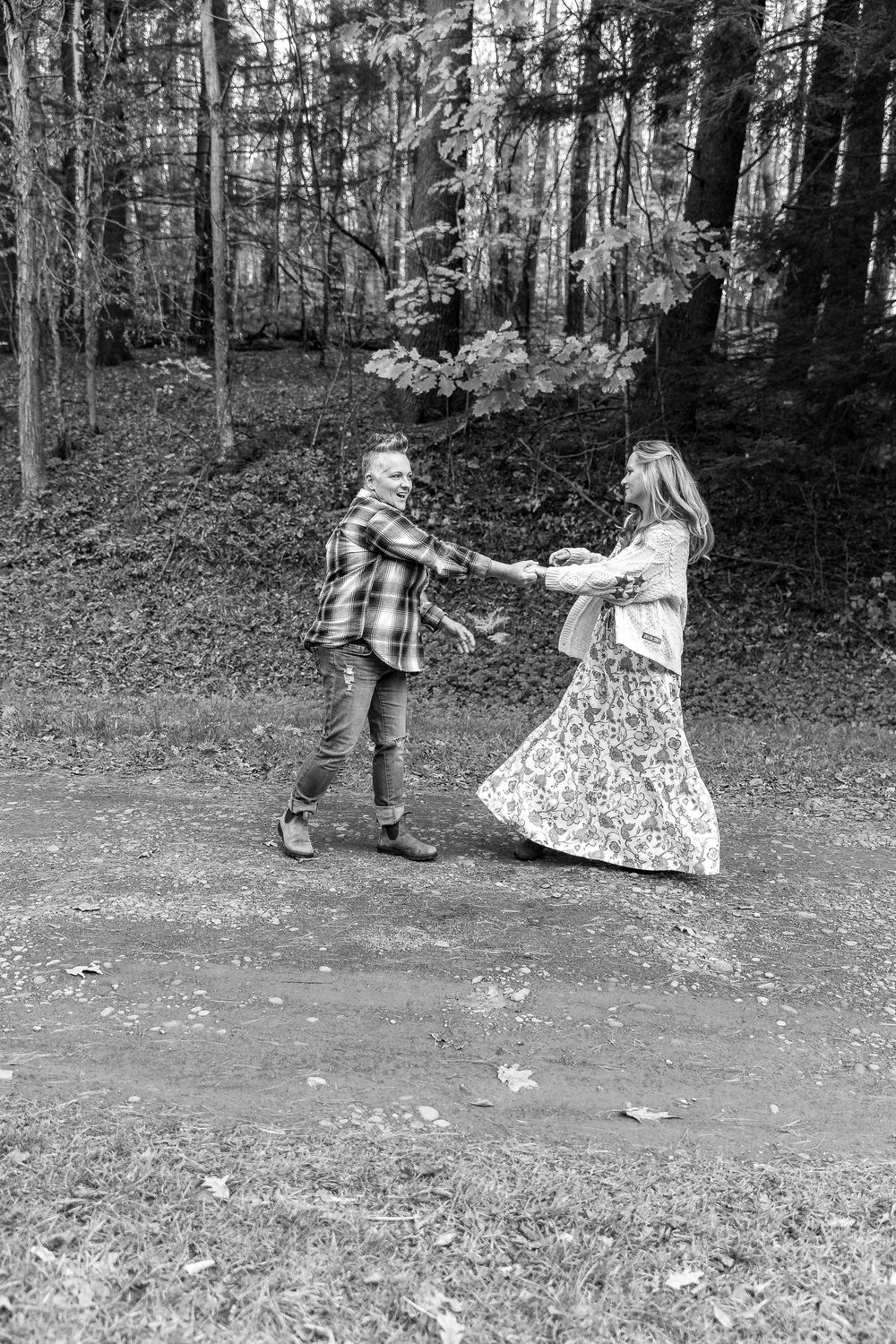 Black and white photo of a joyful couple dancing together in an autumn forest.