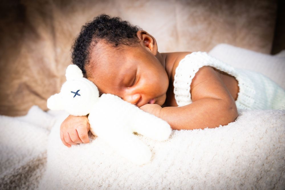 Peaceful newborn baby sleeping on white blanket while cuddling a soft white stuffed bear.