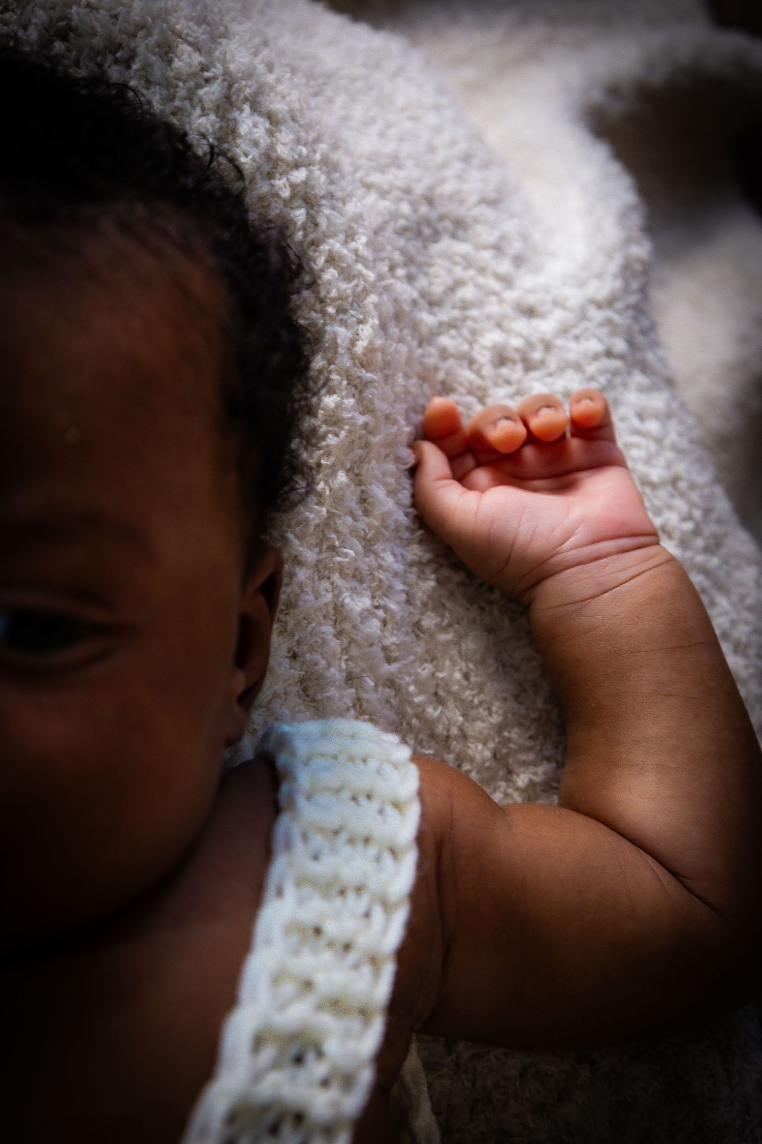 Close-up of a newborn baby's tiny hand resting on a soft white textured blanket.