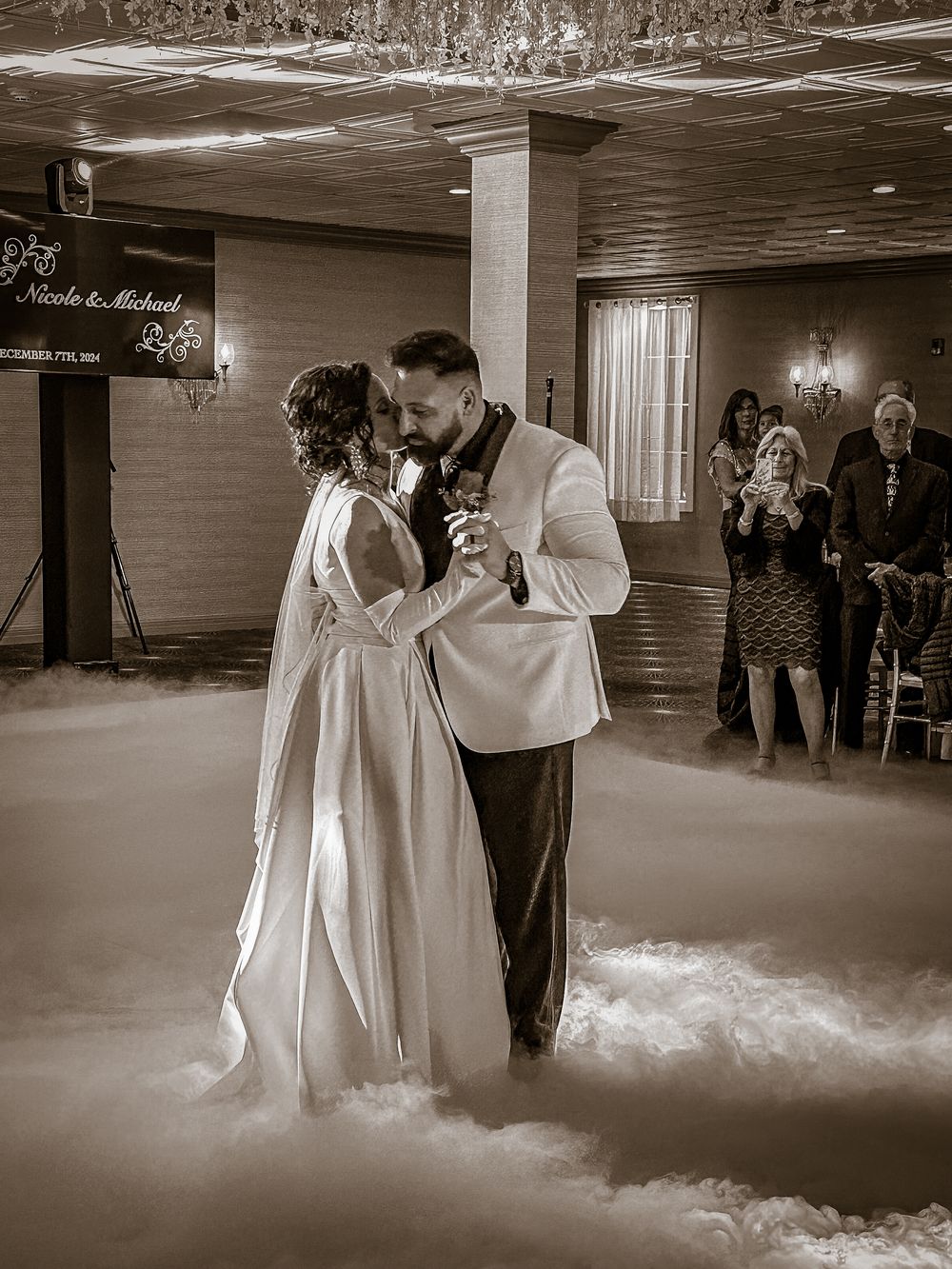 Bride and groom share their first dance surrounded by dramatic fog effects at a elegant wedding reception.