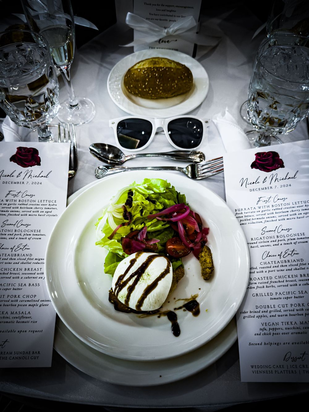 Elegant wedding reception place setting with gourmet salad course and personalized menu cards on white tablecloth.