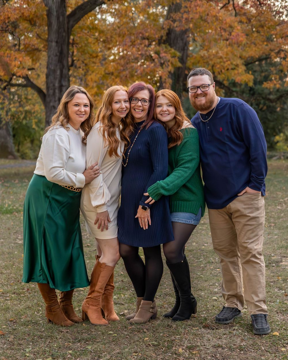 A group of friends pose together outdoors on an autumn day with fall foliage in the background.