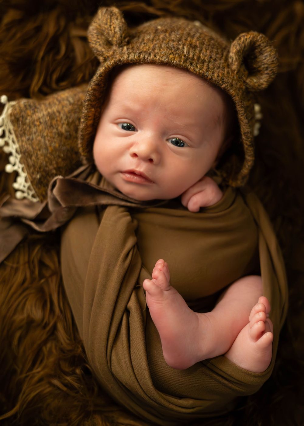 A series of artistic newborn photos showing tiny feet and body parts wrapped in soft brown fabric and textured materials.